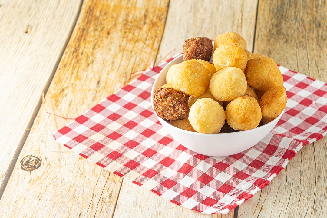 Salgadinhos de festa brasileiros, mistura de petiscos de festa tradicional com coxinha, kibe e outros petiscos fritos sobre mesa de madeira em um recipiente branco.