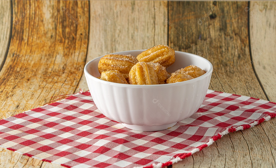 Mini churros brasileiro, um lanche tradicional para festa com açúcar e canela em pó em um recipiente branco e fundo de madeira.