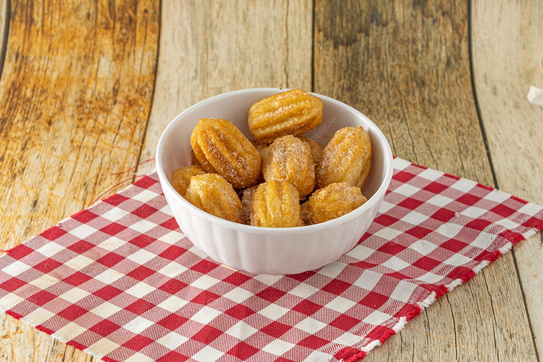 Mini churros brasileiro, um lanche tradicional para festa com açúcar e canela em pó em um recipiente branco e fundo de madeira.