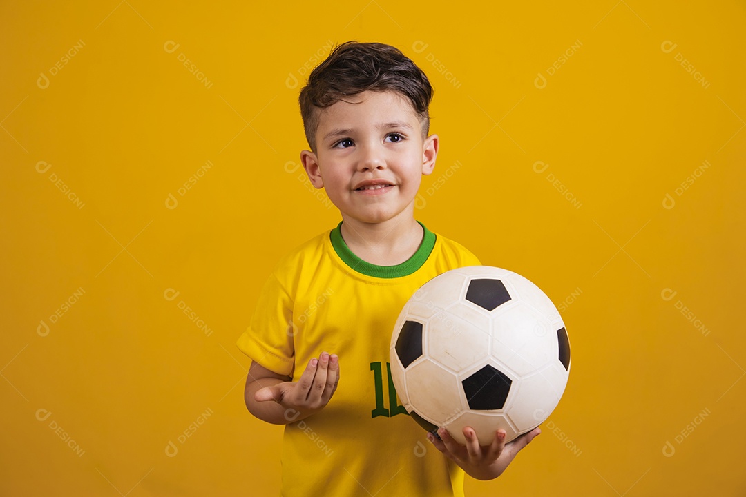 Criança vestida com camiseta do Brasil segurando uma bola de futebol