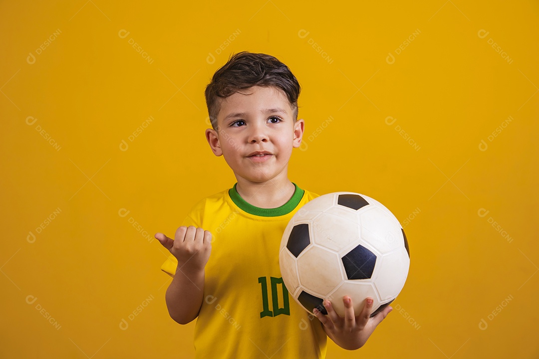 Criança vestida com camiseta do Brasil segurando uma bola de futebol