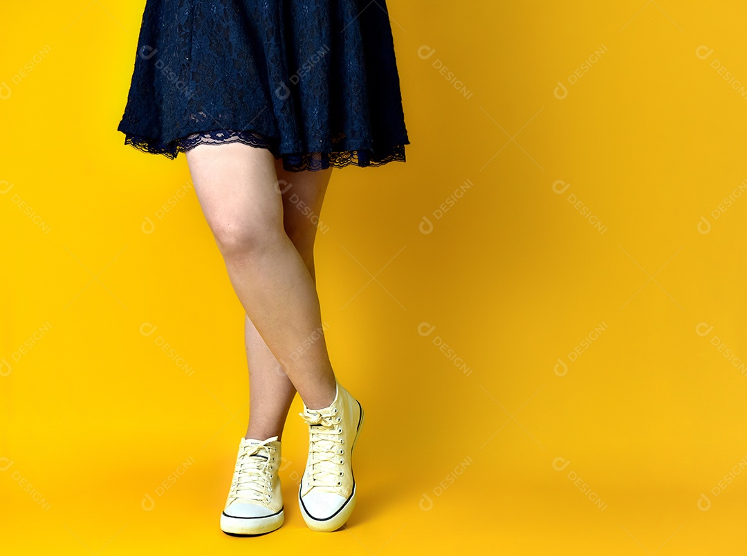 Pernas de menina com vestido azul sobre fundo amarelo.