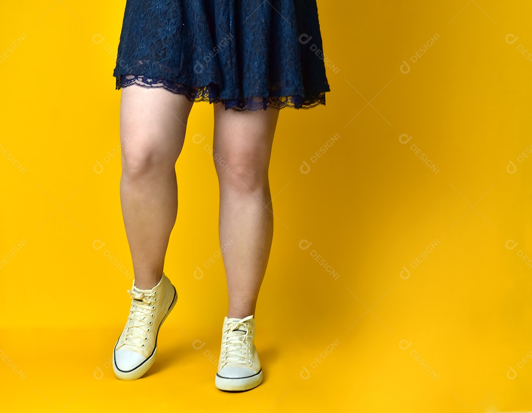 Pernas de menina com vestido azul sobre fundo amarelo.