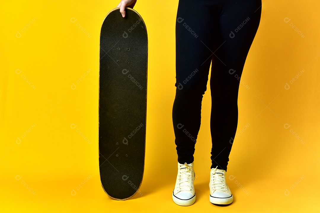 Pernas de garota skatista usando tênis branco sobre fundo amarelo.