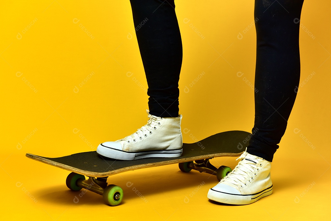 Pernas de garota skatista usando tênis branco sobre fundo amarelo.