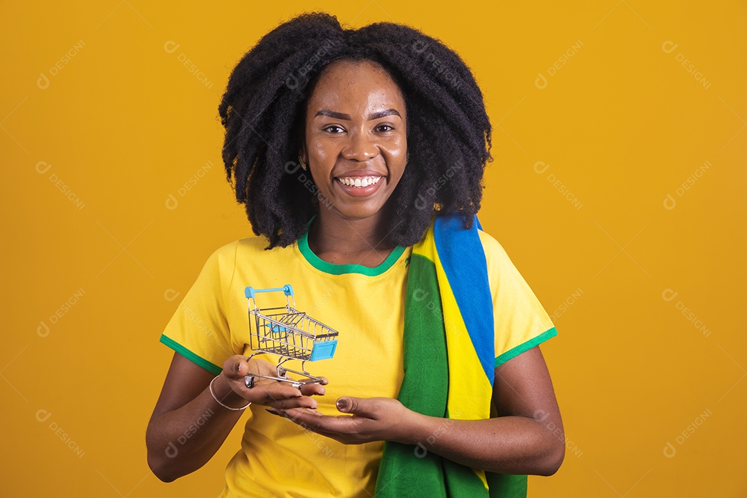 Mulher afro-brasileira vestindo camiseta do Brasil segurando um carrinho de compras