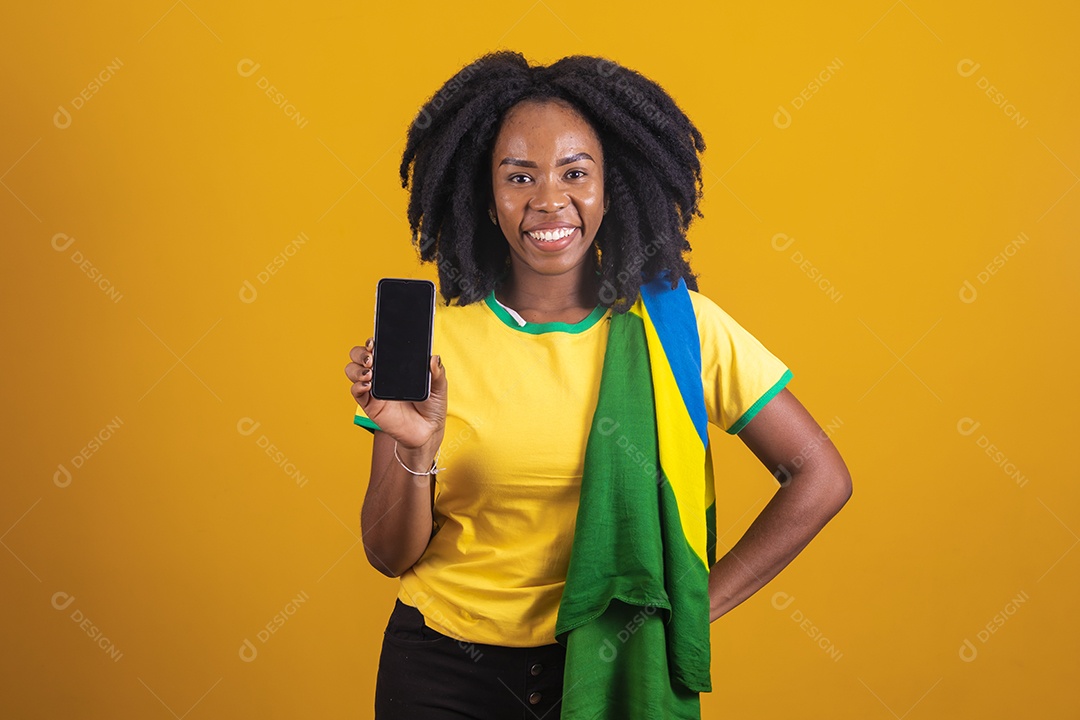 Mulher afro-brasileira vestindo camiseta do Brasil segurando um celular smartphone