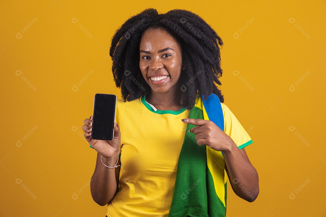 Mulher afro-brasileira vestindo camiseta do Brasil segurando um celular smartphone