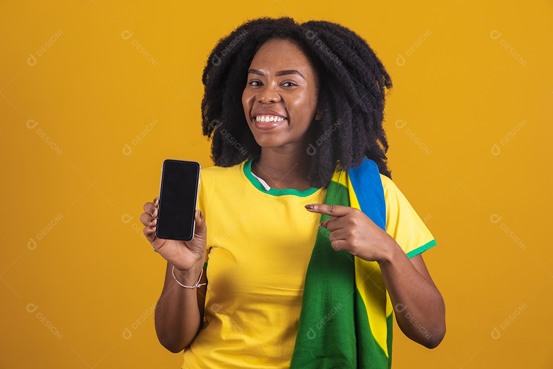 Mulher afro-brasileira vestindo camiseta do Brasil segurando um celular smartphone