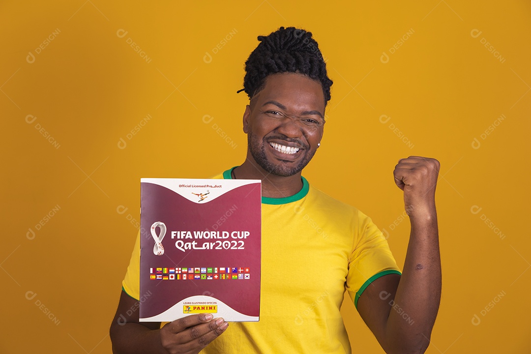 Homem brasileiro vestindo uma camiseta do Brasil e segurando um álbum da FIFA