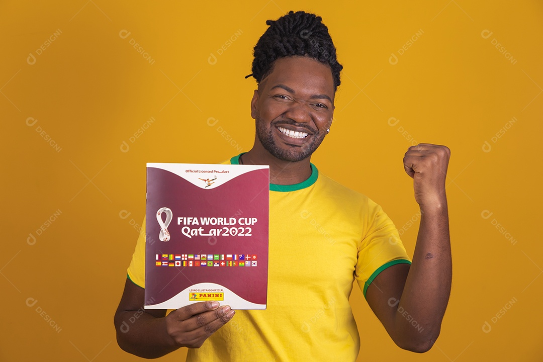 Homem brasileiro vestindo uma camiseta do Brasil e segurando um álbum da FIFA