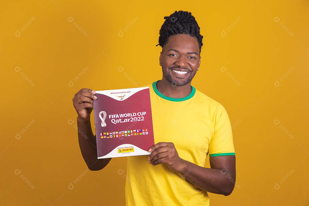 Homem brasileiro vestindo uma camiseta do Brasil e segurando um álbum da FIFA