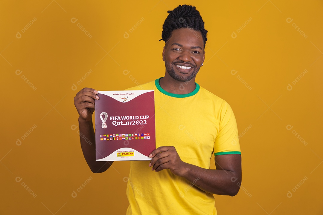 Homem brasileiro vestindo uma camiseta do Brasil e segurando um álbum da FIFA