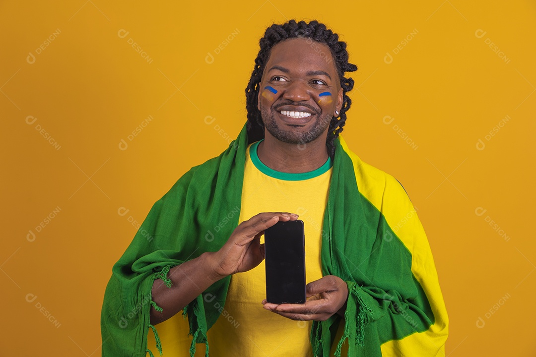 Homem brasileiro vestindo uma camiseta do Brasil e segurando um celular smartphone