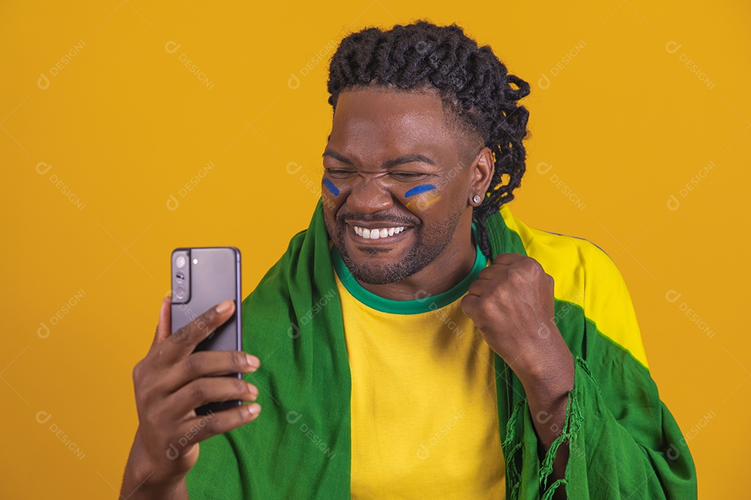 Homem brasileiro vestindo uma camiseta do Brasil e segurando um celular smartphone
