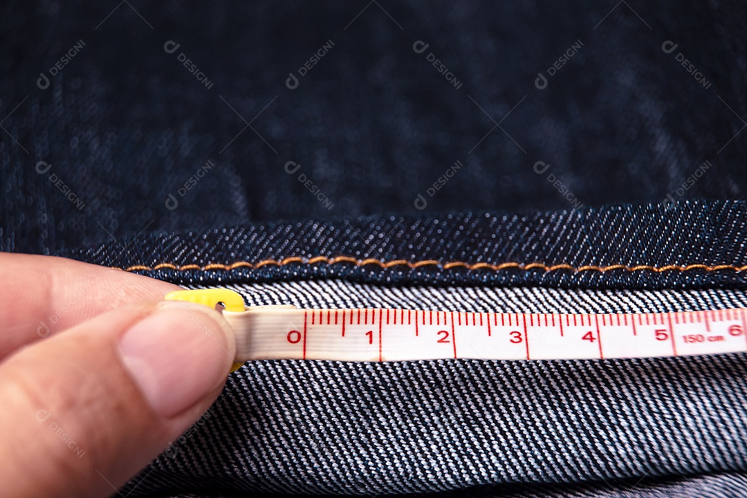 A mão do alfaiate mede o comprimento do jeans com uma medida