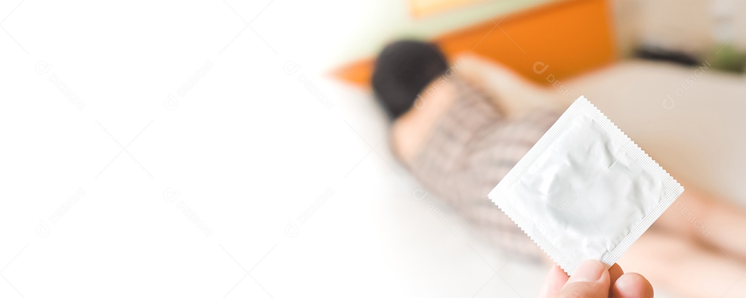 Mão humana segurando um preservativo embalado contra uma mulher turva nas costas