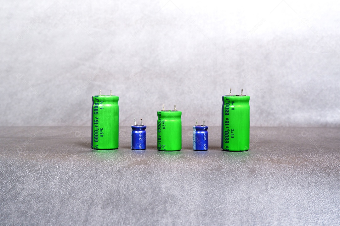 Capacitores eletrolíticos de vários tamanhos são dispostos em fila no chão de cimento