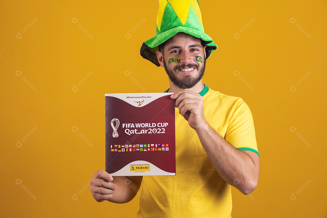 Homem brasileiro vestindo uma camiseta do Brasil e segurando um álbum da fifa