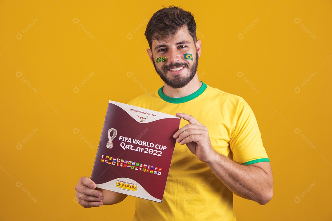 Homem brasileiro vestindo uma camiseta do Brasil e segurando um álbum da copa