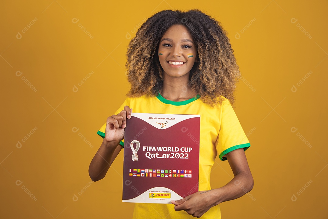 Mulher afro-brasileira vestindo camiseta do Brasil segurando álbum copa do mundo