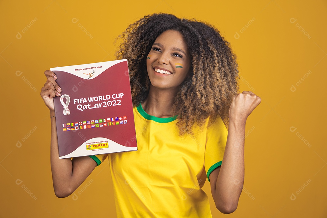 Mulher afro-brasileira vestindo camiseta do Brasil segurando álbum copa do mundo