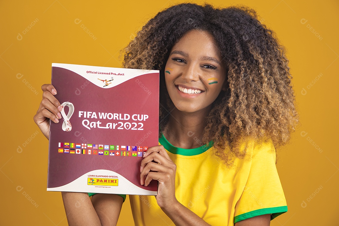 Mulher afro-brasileira vestindo camiseta do Brasil segurando álbum copa do mundo
