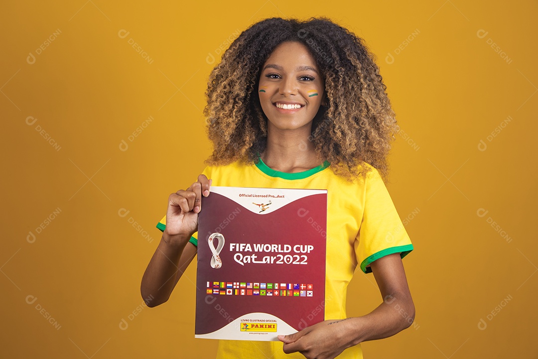 Mulher afro-brasileira vestindo camiseta do Brasil segurando álbum copa do mundo