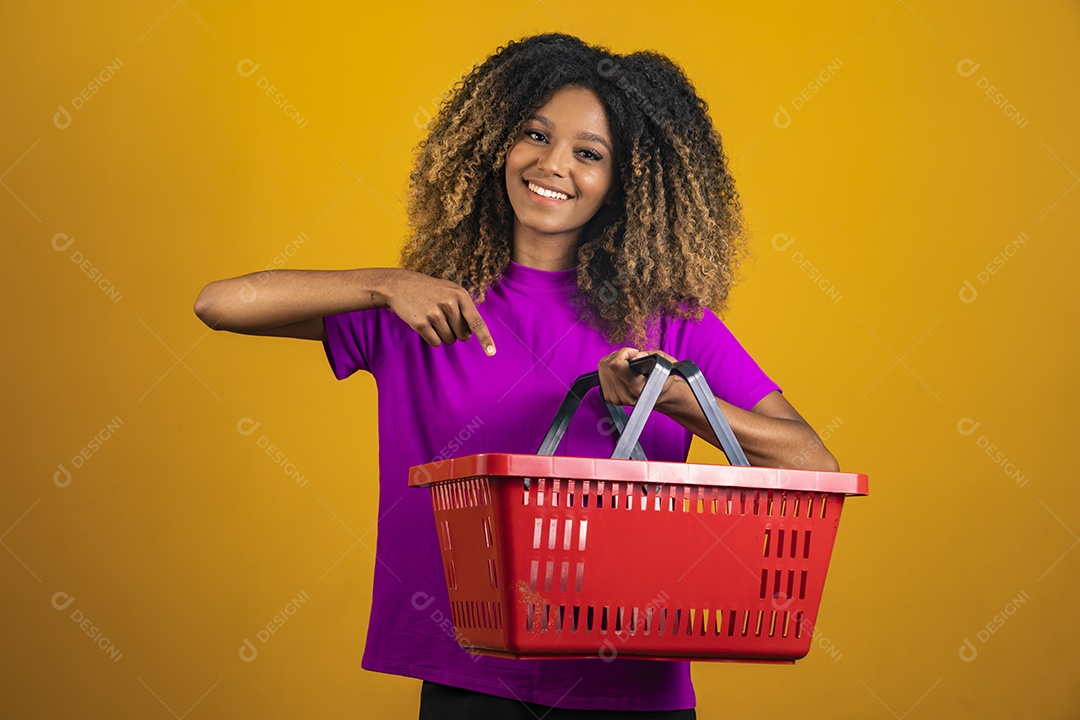 Linda mulher jovem morena cabelo cacheado segurando cestas mercado sobre fundo isolado amarelo