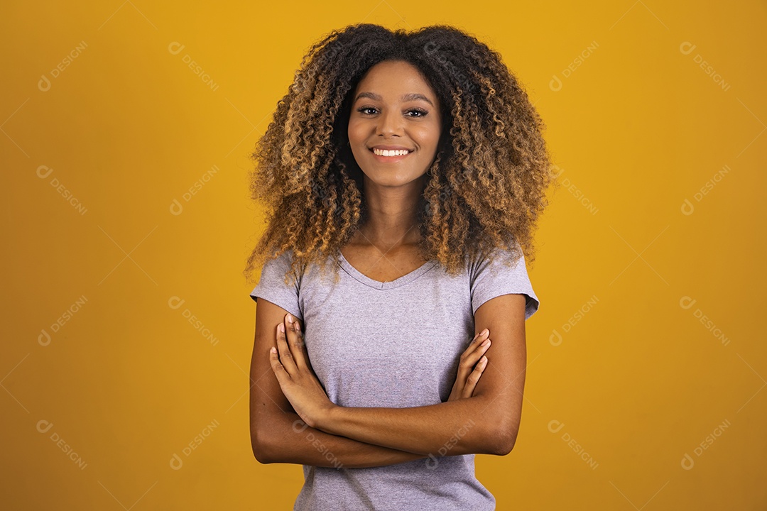 Linda mulher jovem morena cabelo afro braços cruzados sobre fundo isolado amarelo
