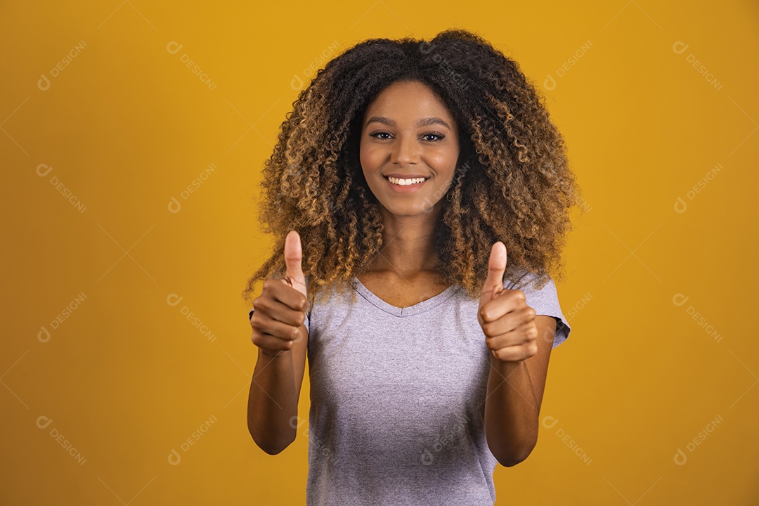 Linda mulher jovem morena cabelo afro gestos mãos polegar para cima sobre fundo isolado amarelo
