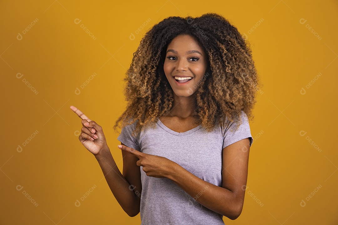 Linda mulher jovem morena cabelo afro apontando para lado sobre fundo isolado amarelo