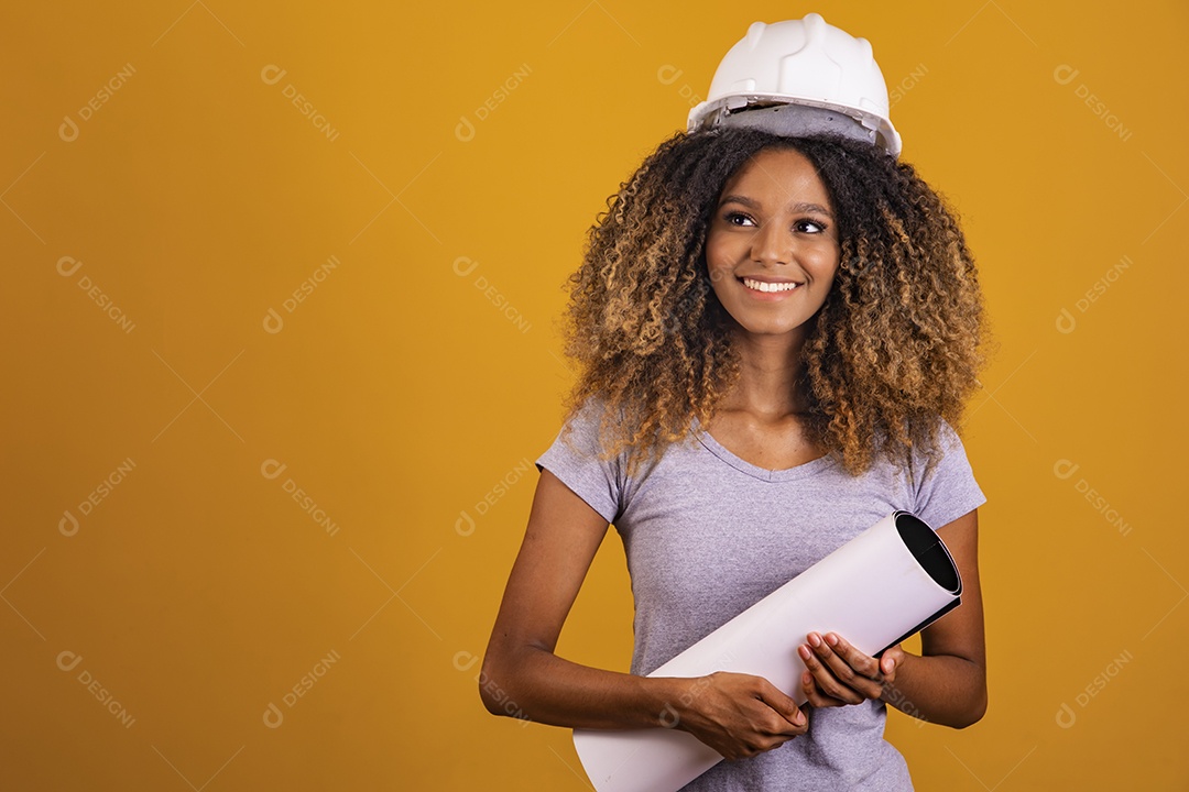 Linda mulher jovem engenheira usando capacete branco morena cabelo afro segurando projeto sobre fundo isolado amarelo
