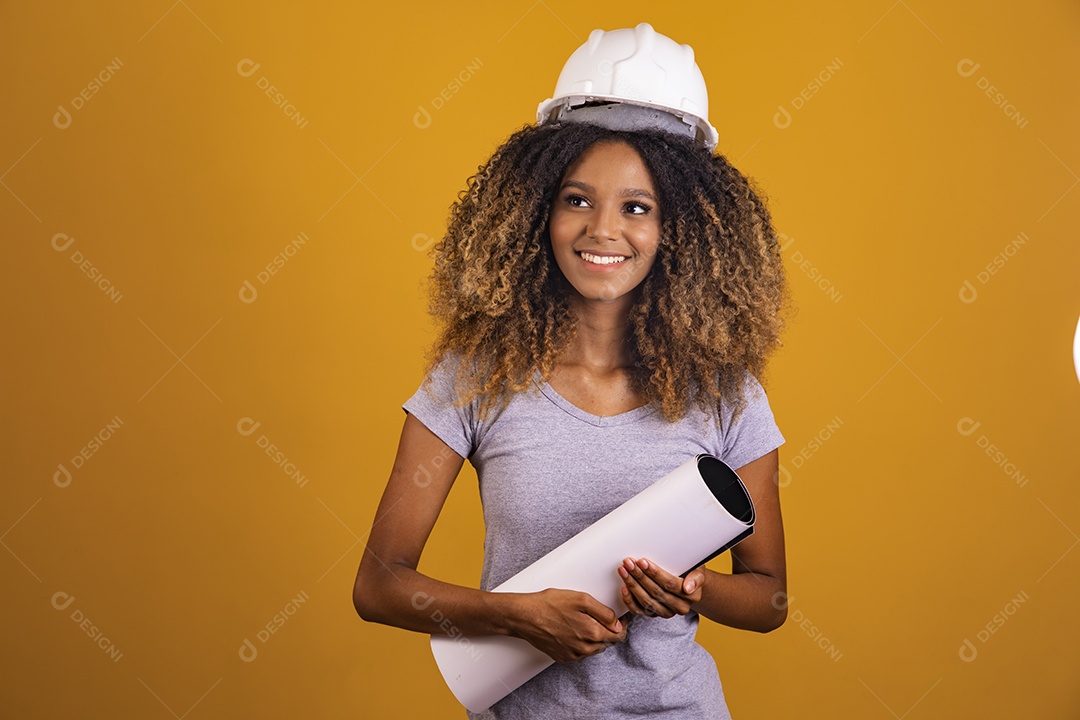 Linda mulher jovem engenheira usando capacete branco morena cabelo afro segurando projeto sobre fundo isolado amarelo