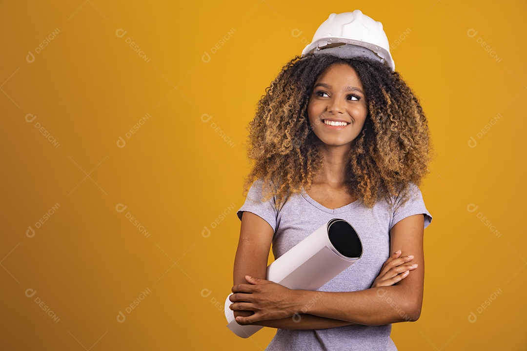 Linda mulher jovem engenheira usando capacete branco morena cabelo afro segurando projeto sobre fundo isolado amarelo