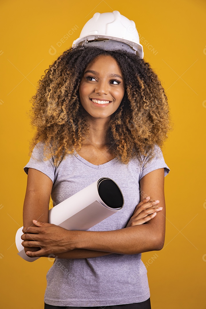 Linda mulher jovem engenheira usando capacete branco morena cabelo afro segurando projeto sobre fundo isolado amarelo