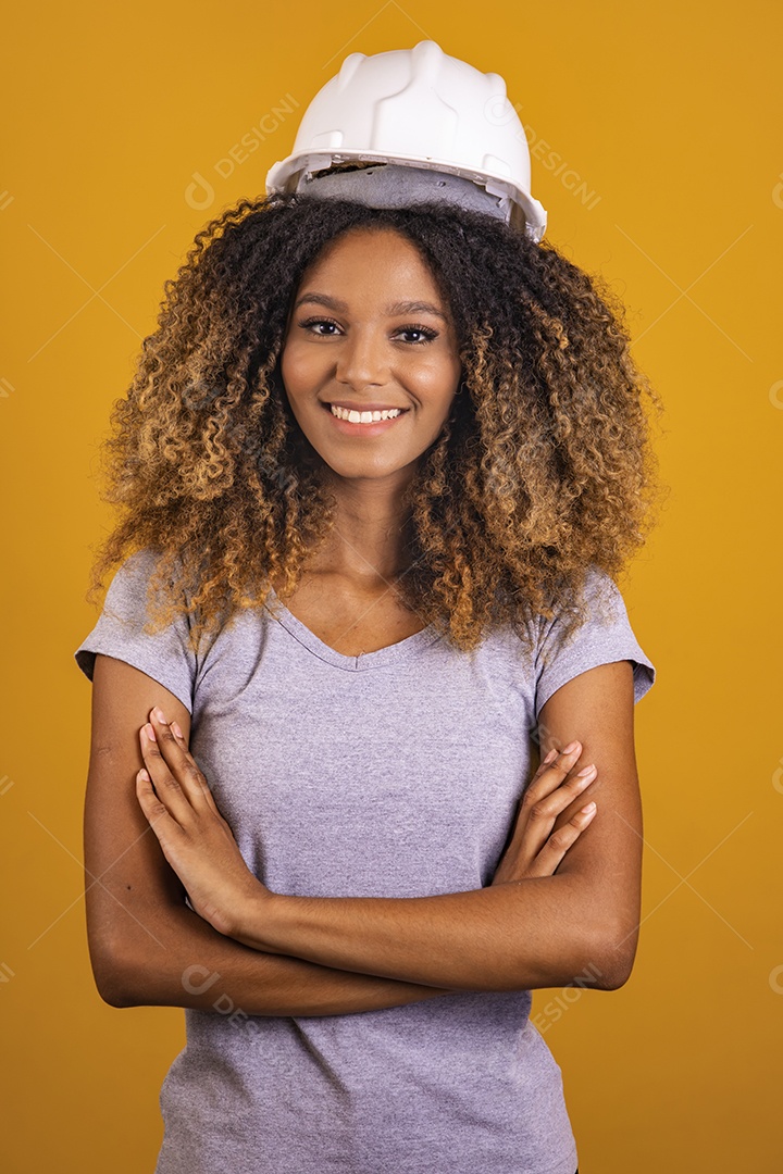 Linda mulher jovem engenheira usando capacete branco morena cabelo afro sobre fundo isolado amarelo