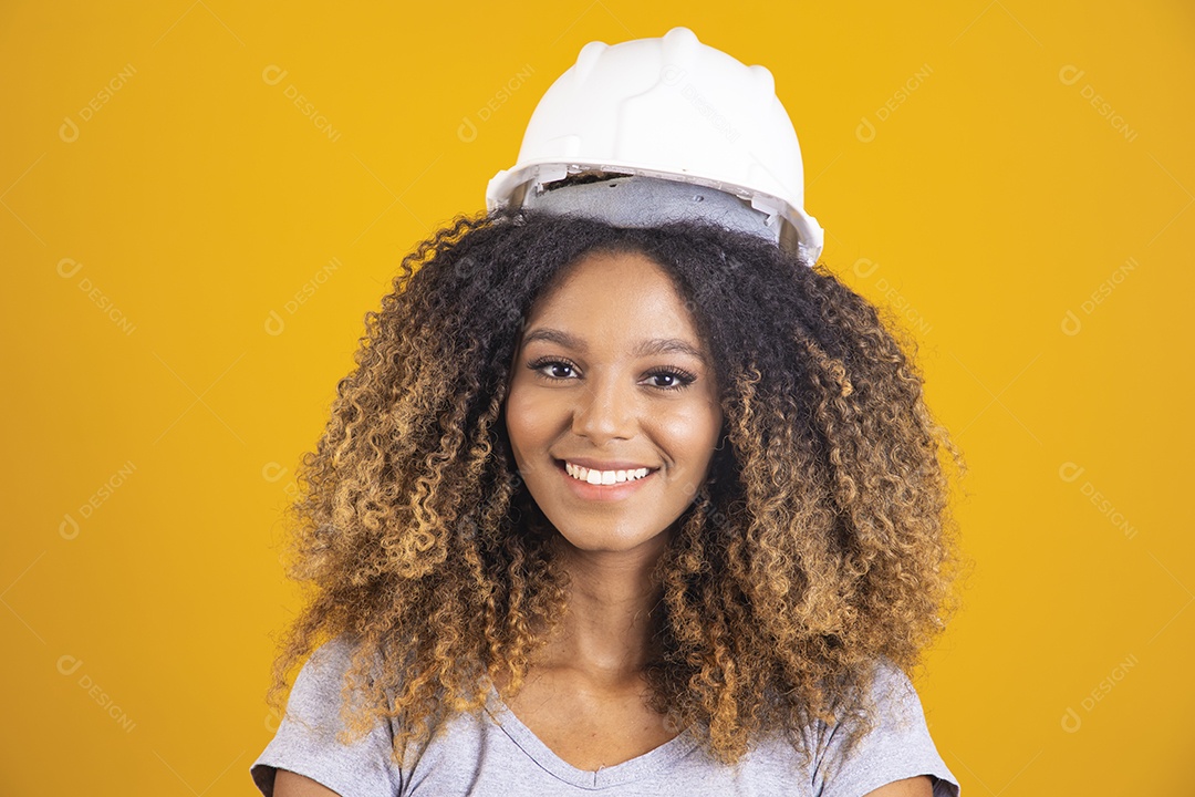 Linda mulher jovem engenheira usando capacete branco morena cabelo afro segurando projeto sobre fundo isolado amarelo
