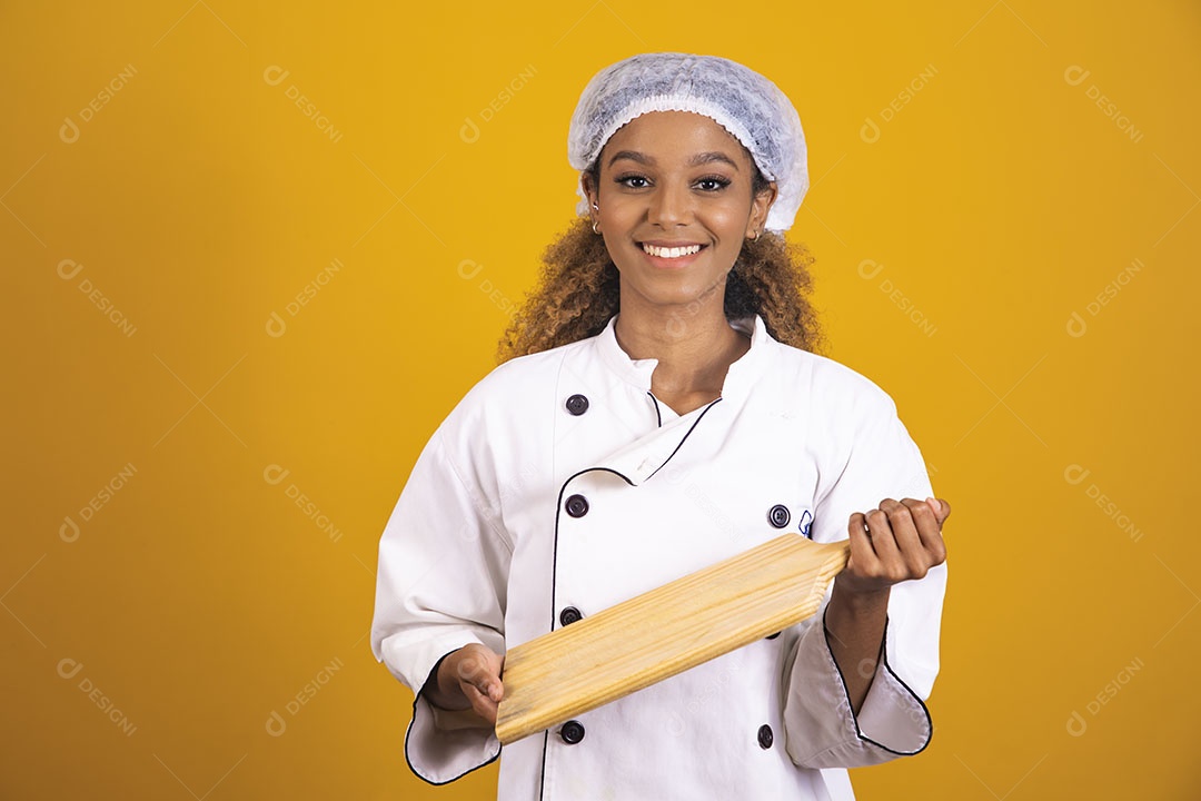 Mulher afro-brasileira usando roupa de chefe segurando um rolo de massas