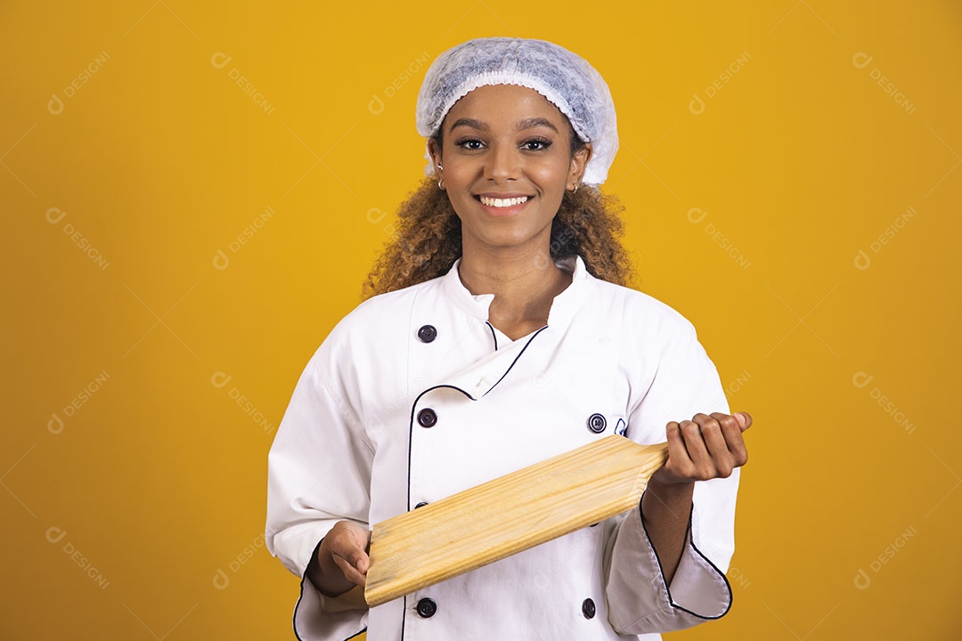 Mulher afro-brasileira usando roupa de chefe segurando um rolo de massas