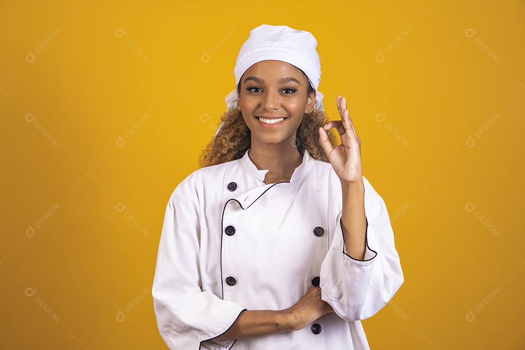 Linda mulher jovem morena cabelo afro usando roupas avental branco cozinheira sobre fundo isolado amarelo