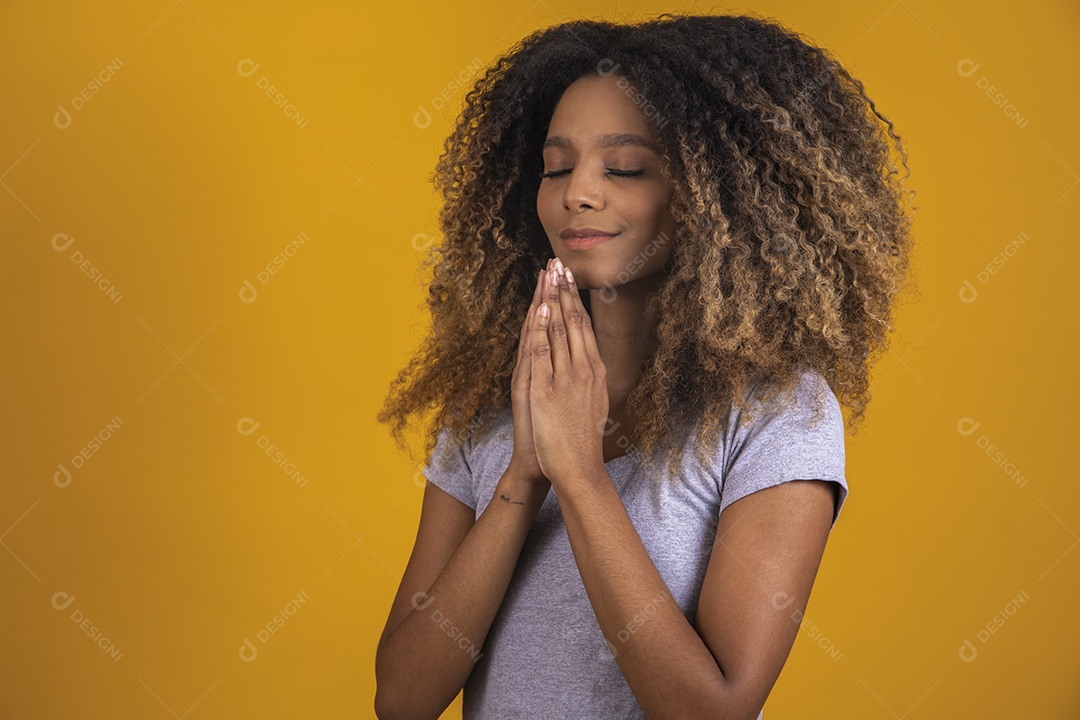 Linda mulher jovem morena cabelo afro expressão orando rezando sobre fundo isolado amarelo