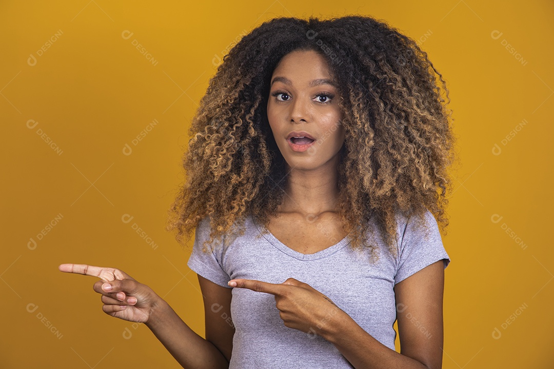 Linda mulher jovem morena cabelo afro apontando para lado sobre fundo isolado amarelo