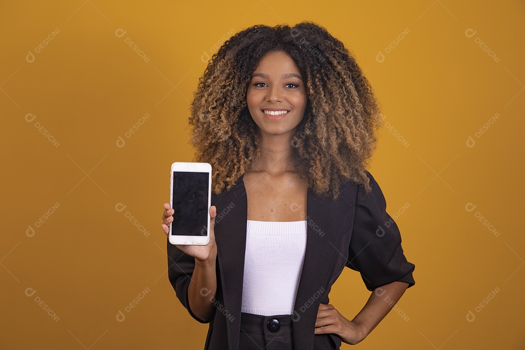 Linda mulher jovem morena cabelo segurando celular smartphone afro sobre fundo isolado amarelo