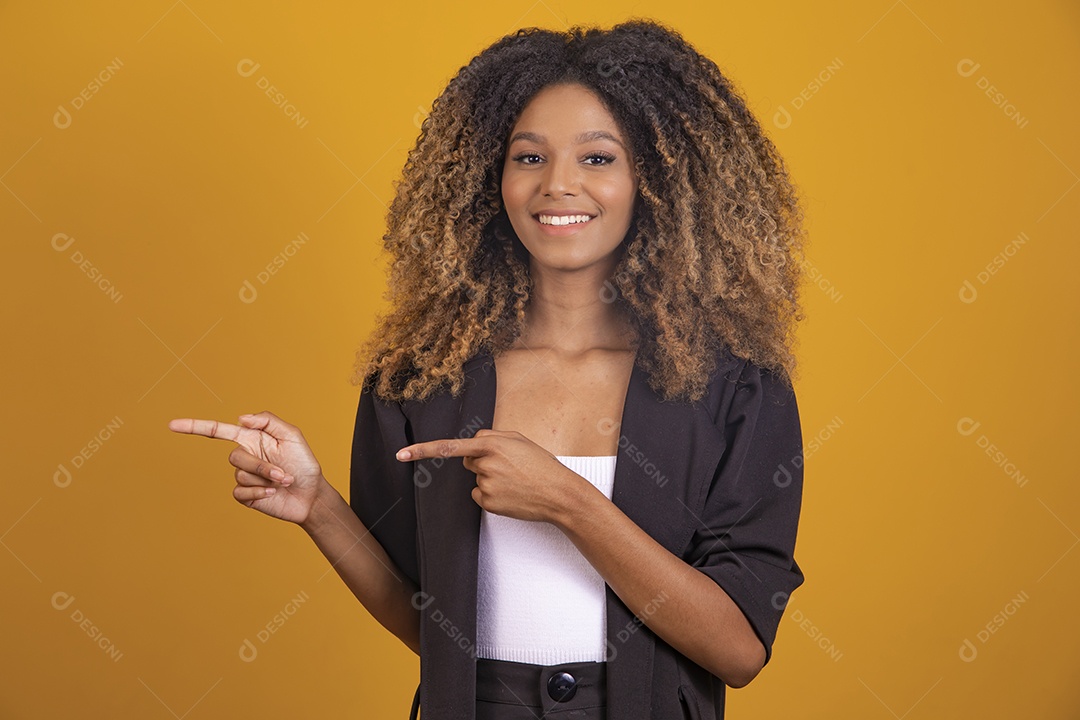 Linda mulher jovem morena cabelo afro apontando para lado sobre fundo isolado amarelo