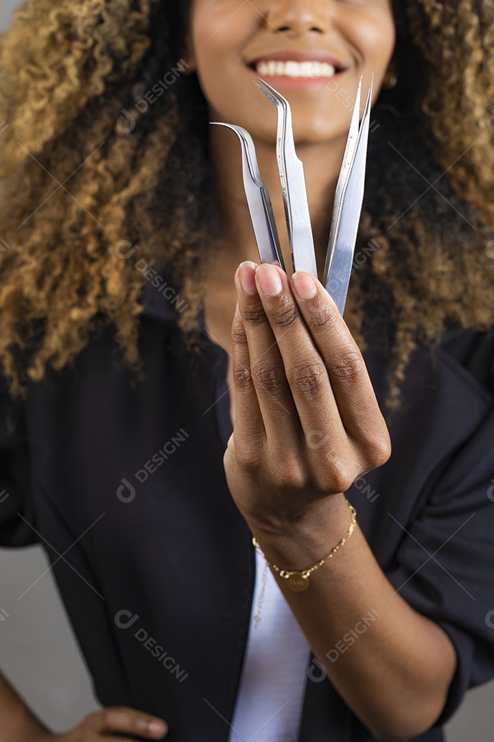 Mulher afro-brasileira vestida formalmente segurando escovinha, pinça e tesoura de sobrancelhas/cílios