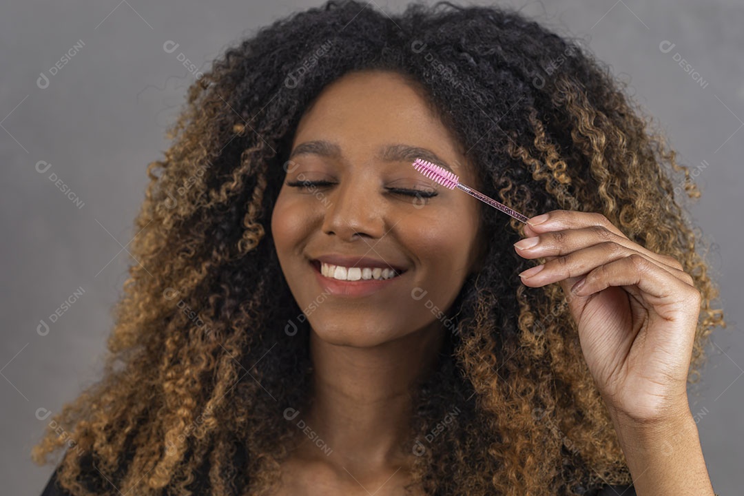 Mulher afro-brasileira vestida formalmente segurando escovinha de sobrancelhas/cílios
