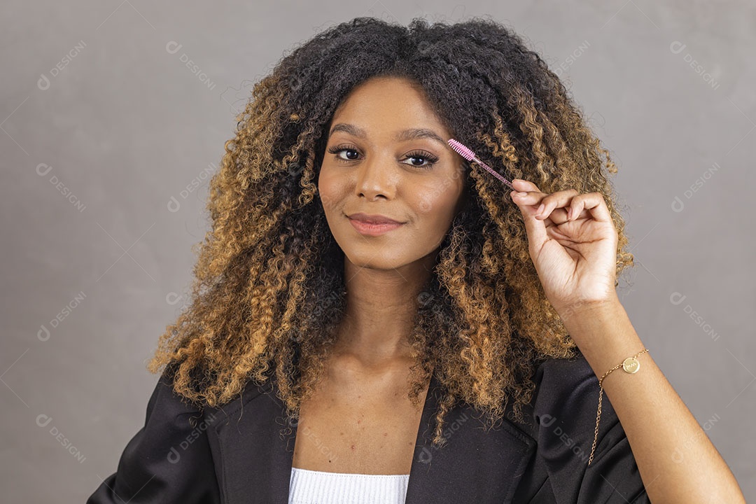 Mulher afro-brasileira vestida formalmente segurando escovinha de sobrancelhas/cílios