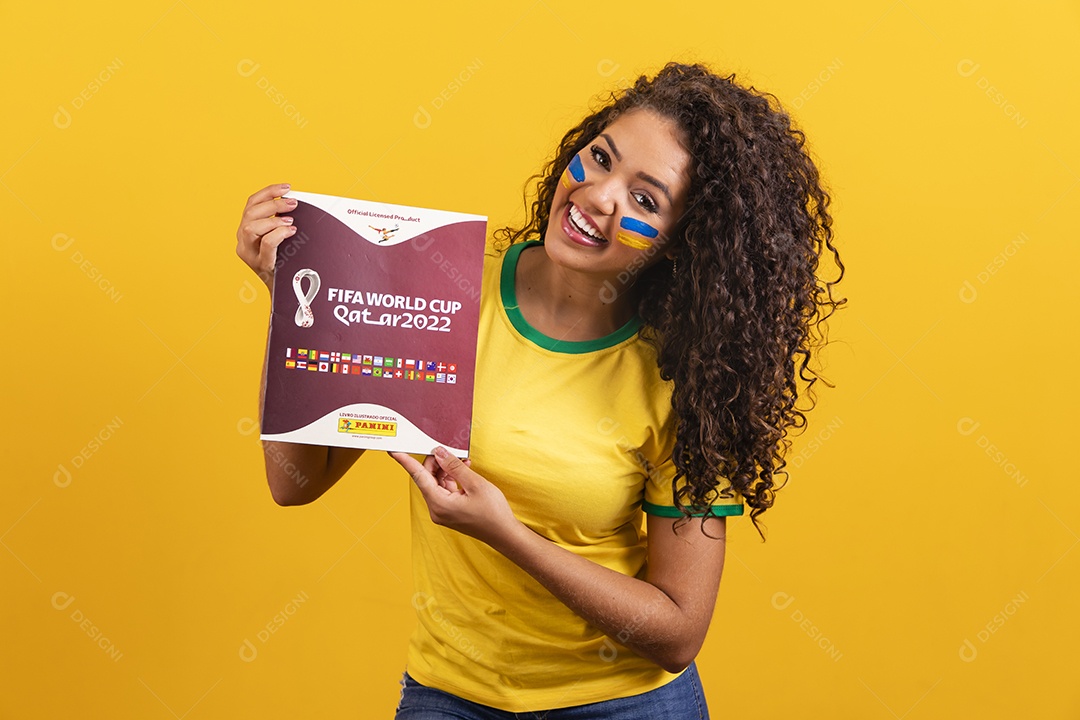 Linda mulher jovem morena segurando álbum da copa do brasil de 2022 futebol cabelo afro sobre fundo isolado amarelo