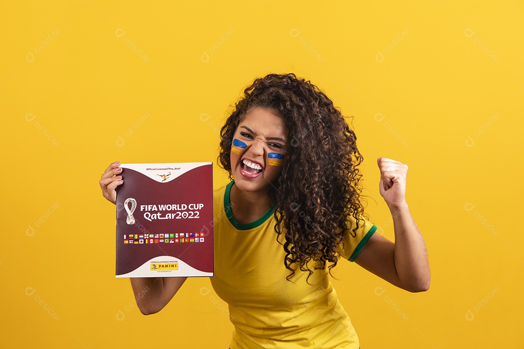 Linda mulher jovem morena segurando álbum da copa do brasil de 2022 futebol cabelo afro sobre fundo isolado amarelo